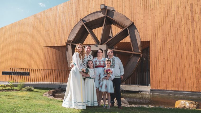 Family in traditional attire poses by a wooden windmill on a sunny day.